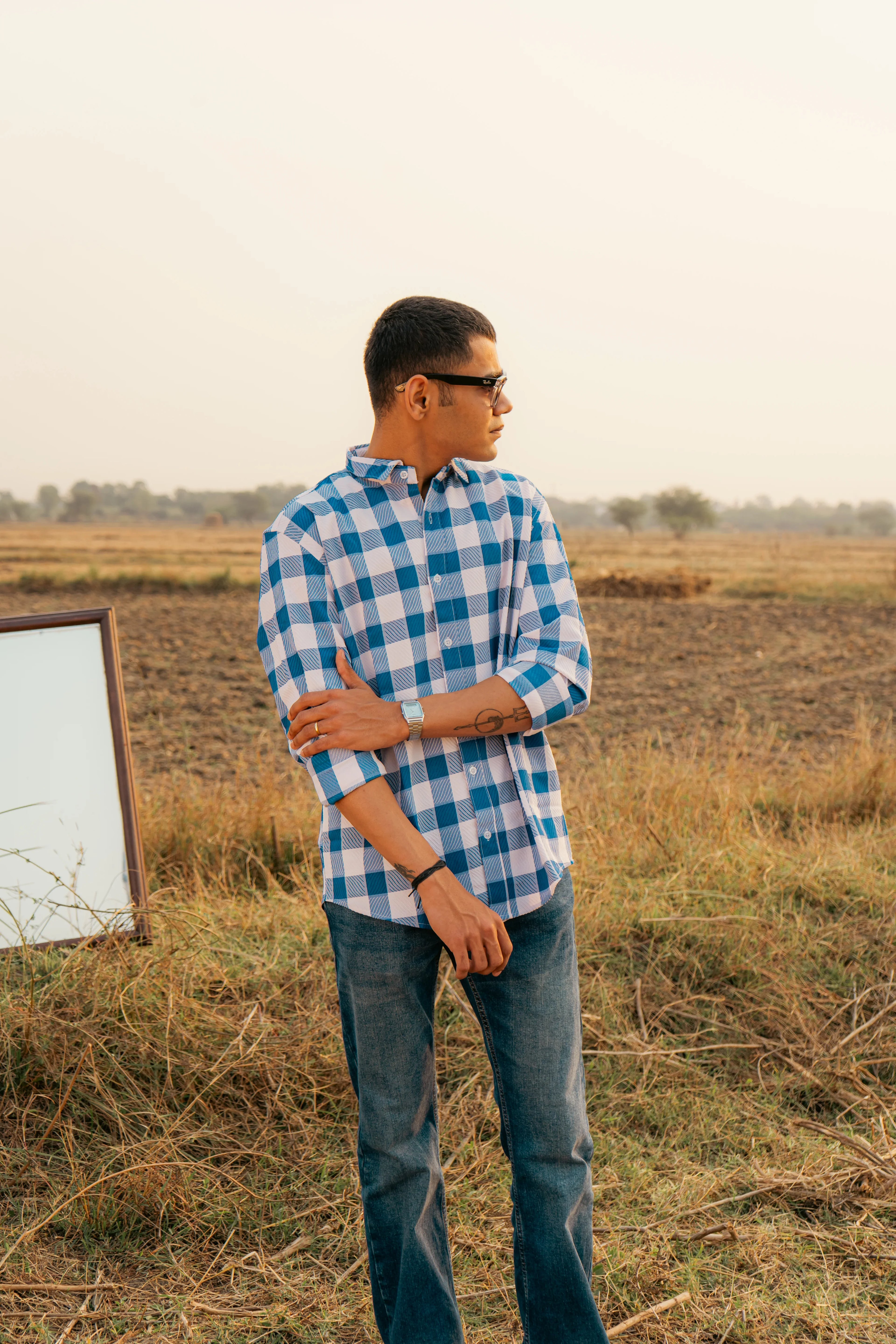 Man in blue checkered shirt and jeans standing in a field at sunset