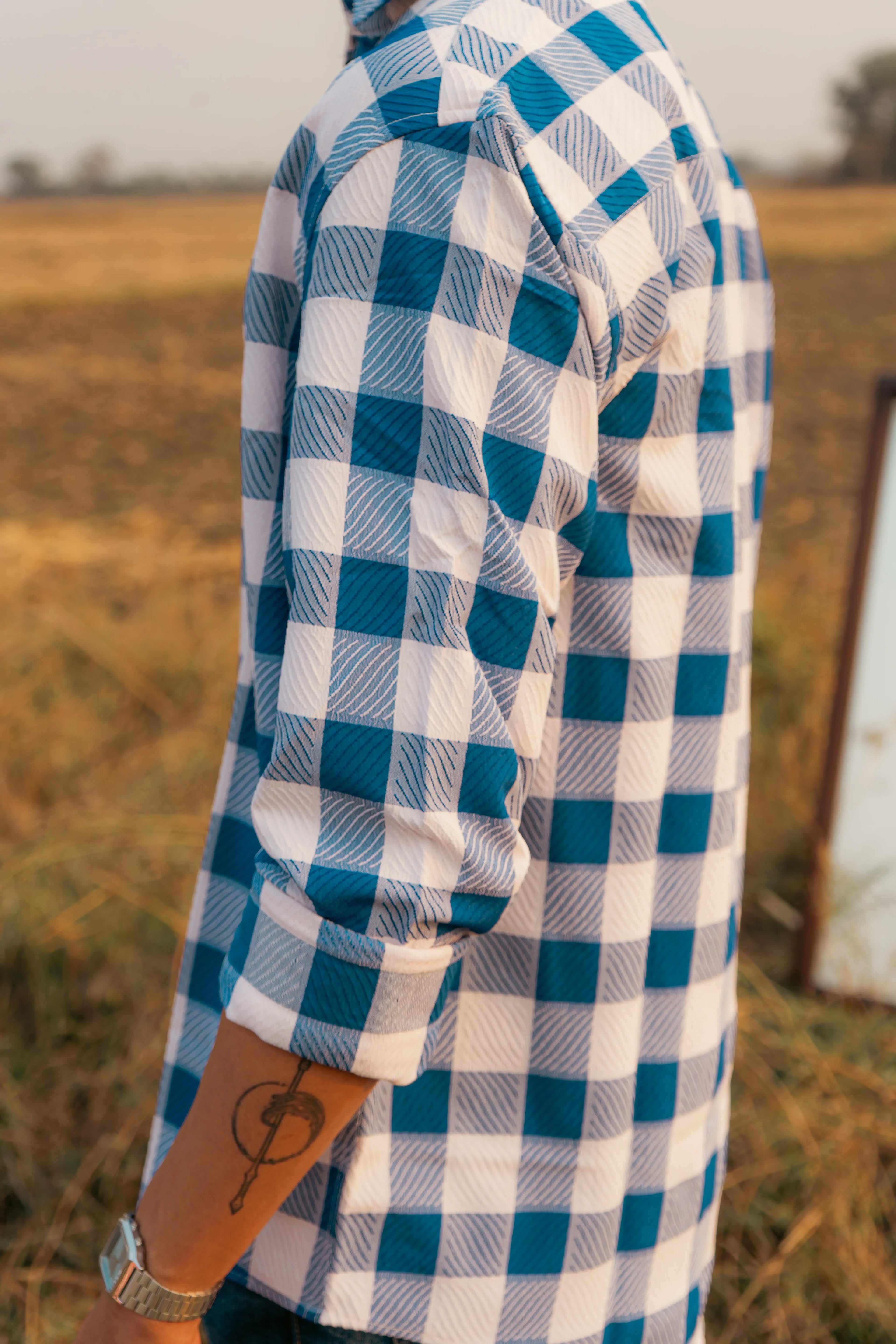 Man wearing blue and white checkered shirt with rolled sleeves outdoors