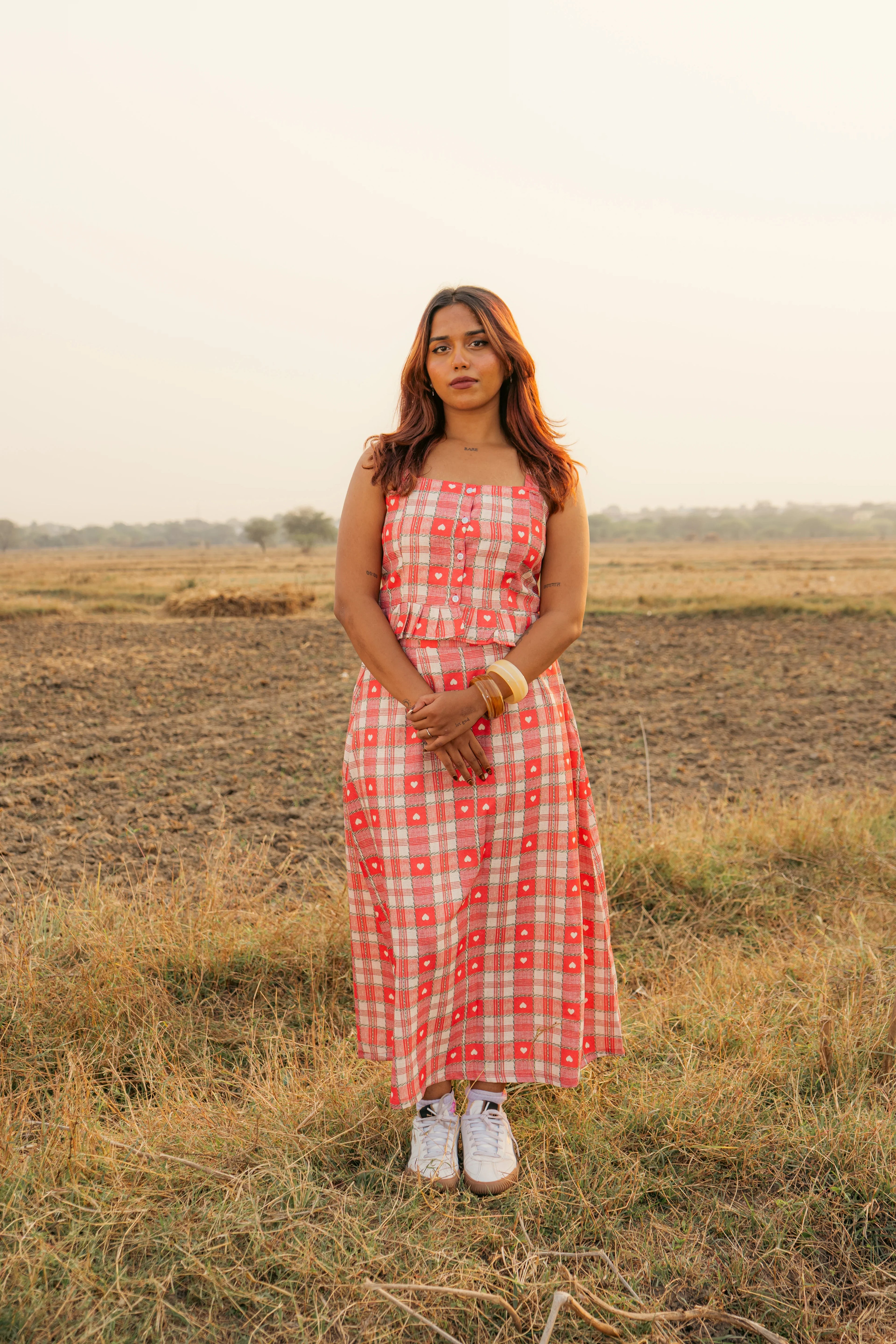Woman in red plaid sleeveless maxi dress standing in a field at sunset