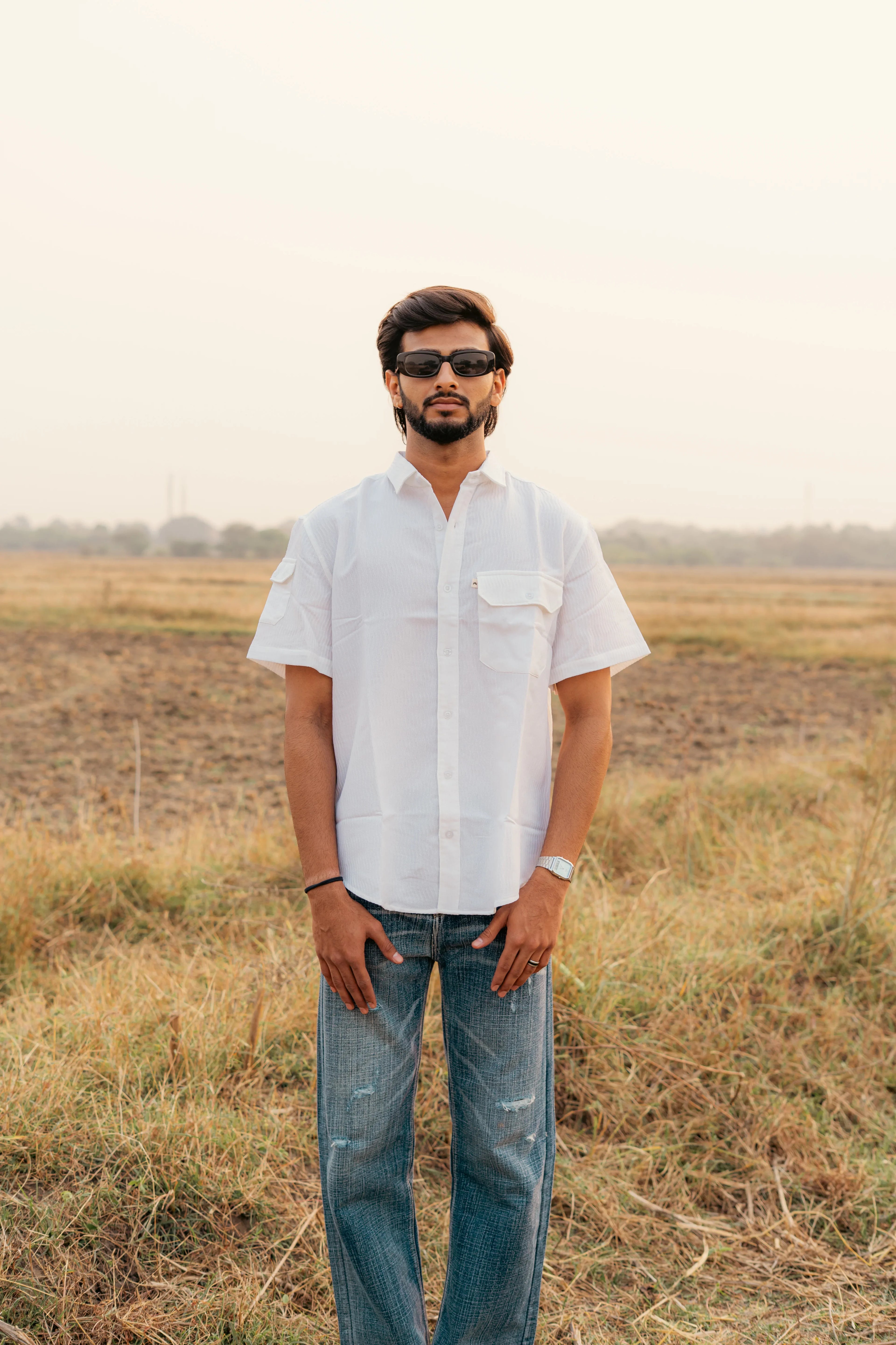 Man in white short sleeve shirt and jeans standing outdoors in a grassy field