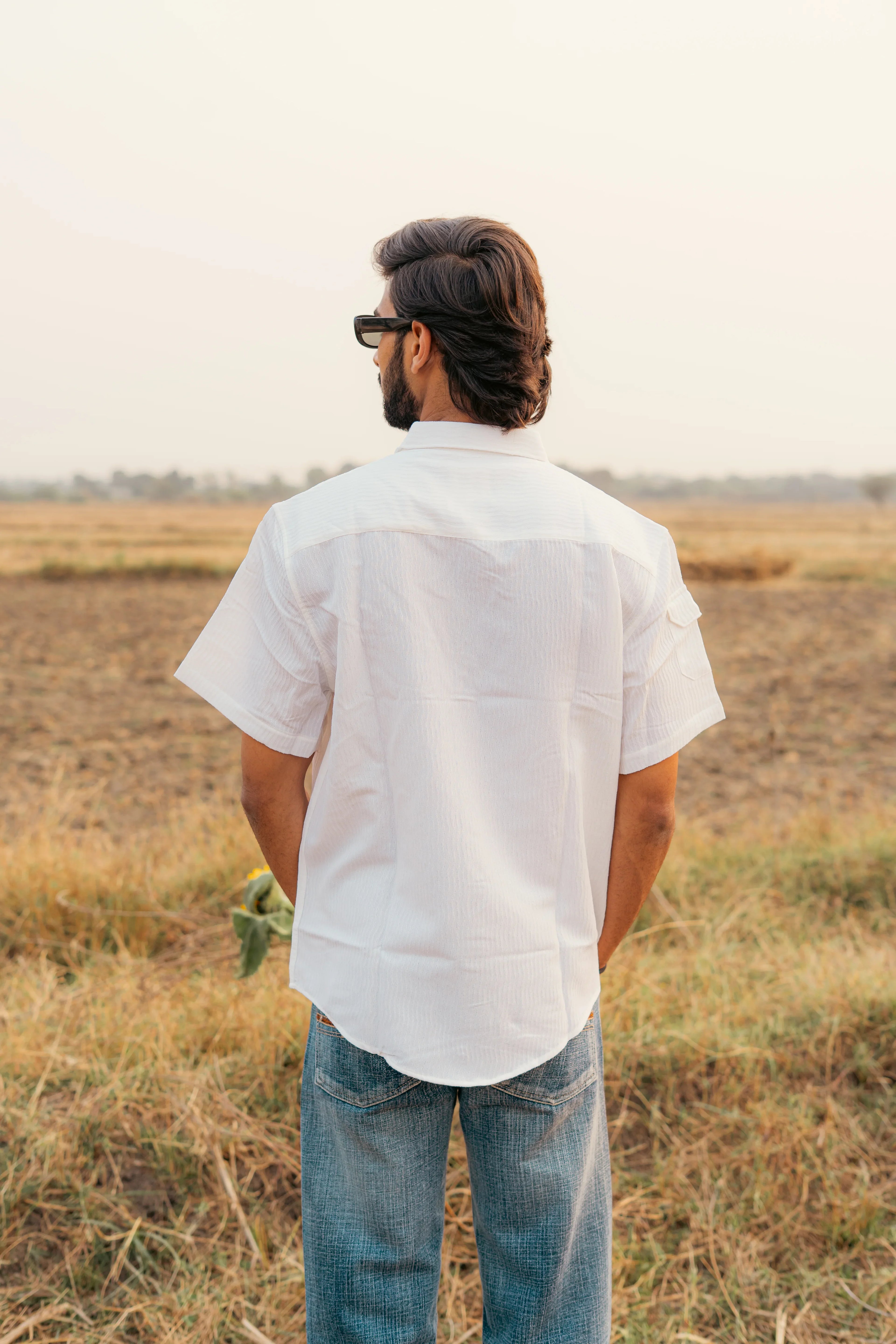 Man in white short sleeve shirt and jeans standing in grassy field, back view