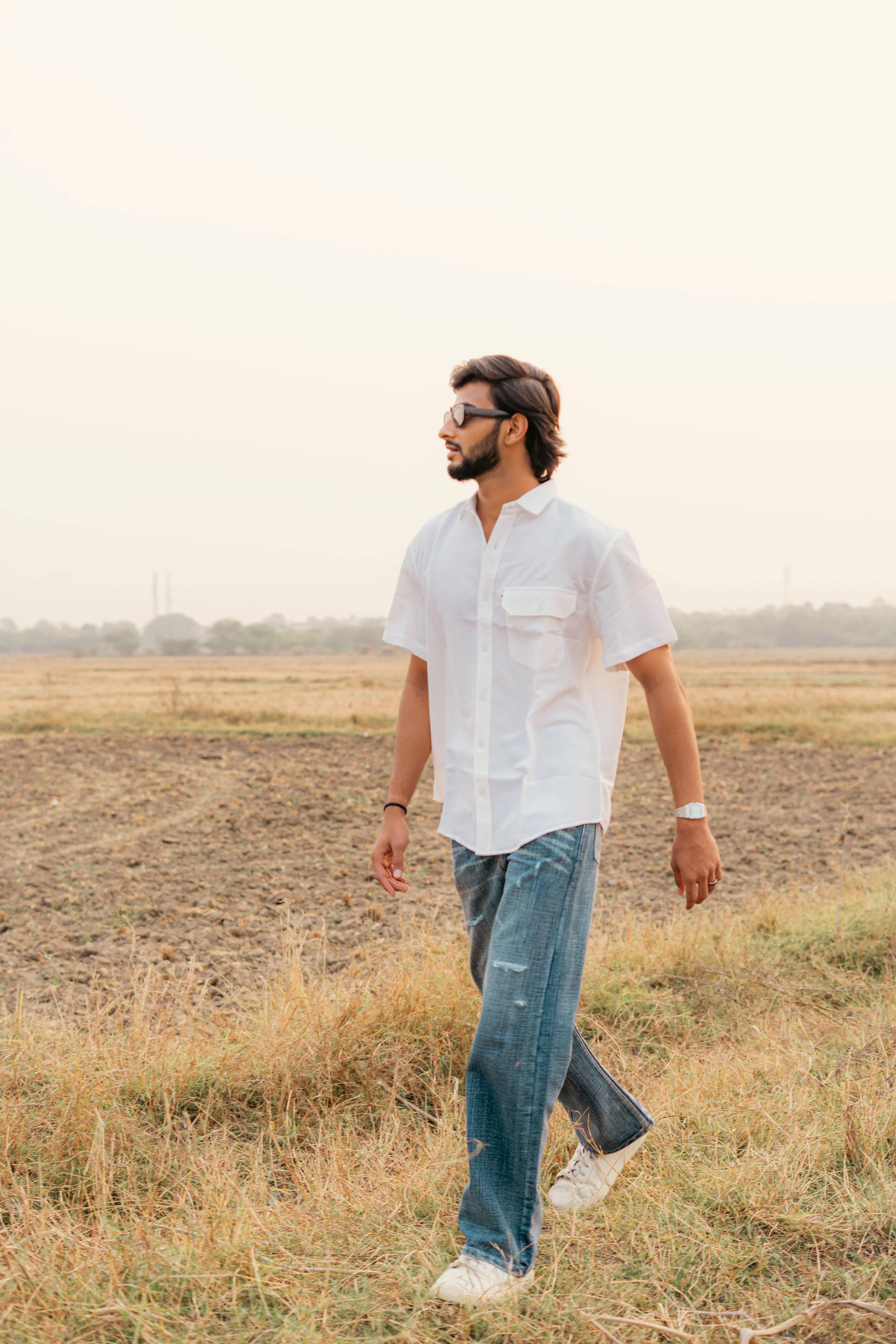 Man in white short sleeve shirt and blue jeans walking outdoors in a field at sunset