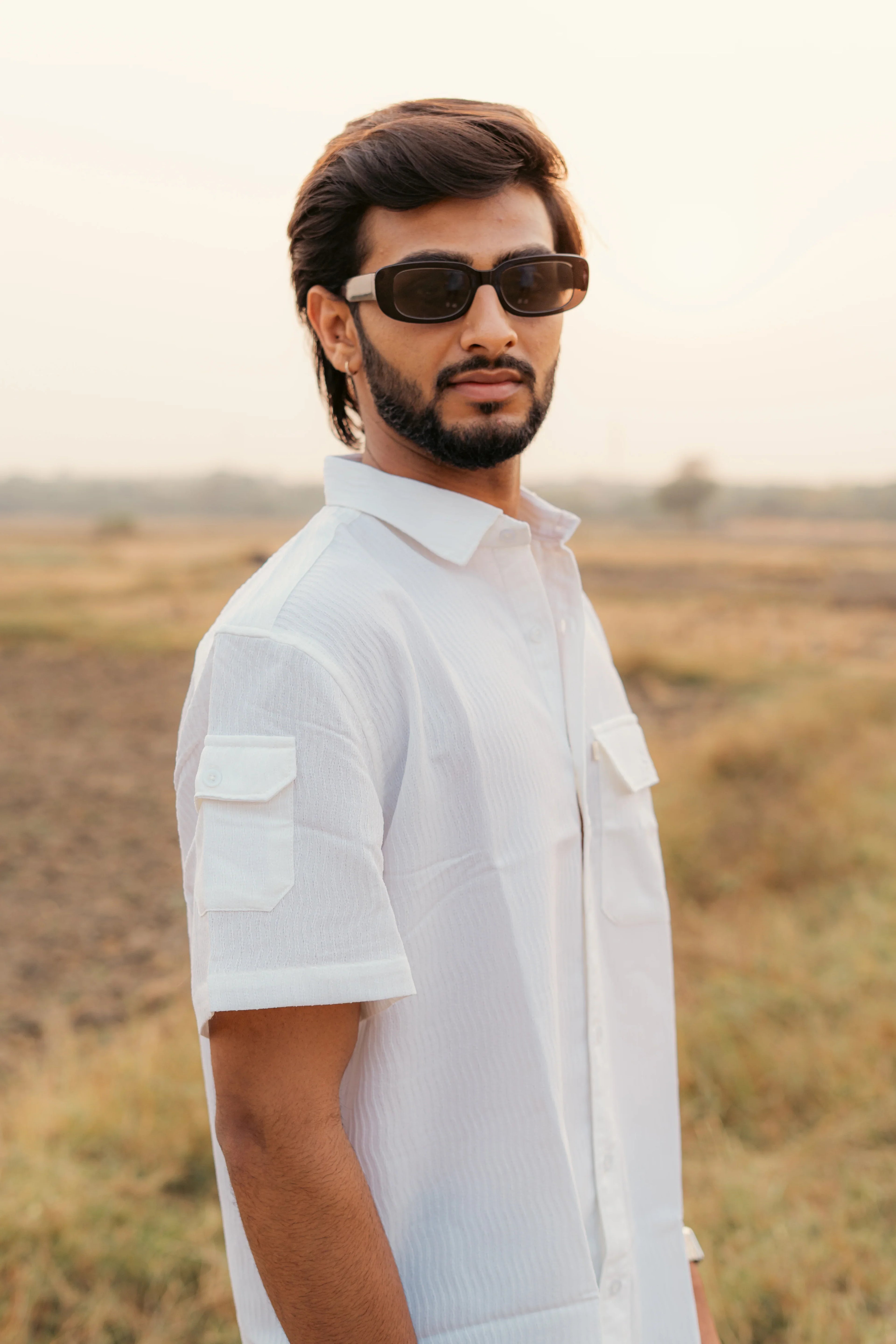 Man wearing a white short sleeve shirt with chest pockets and sunglasses outdoors