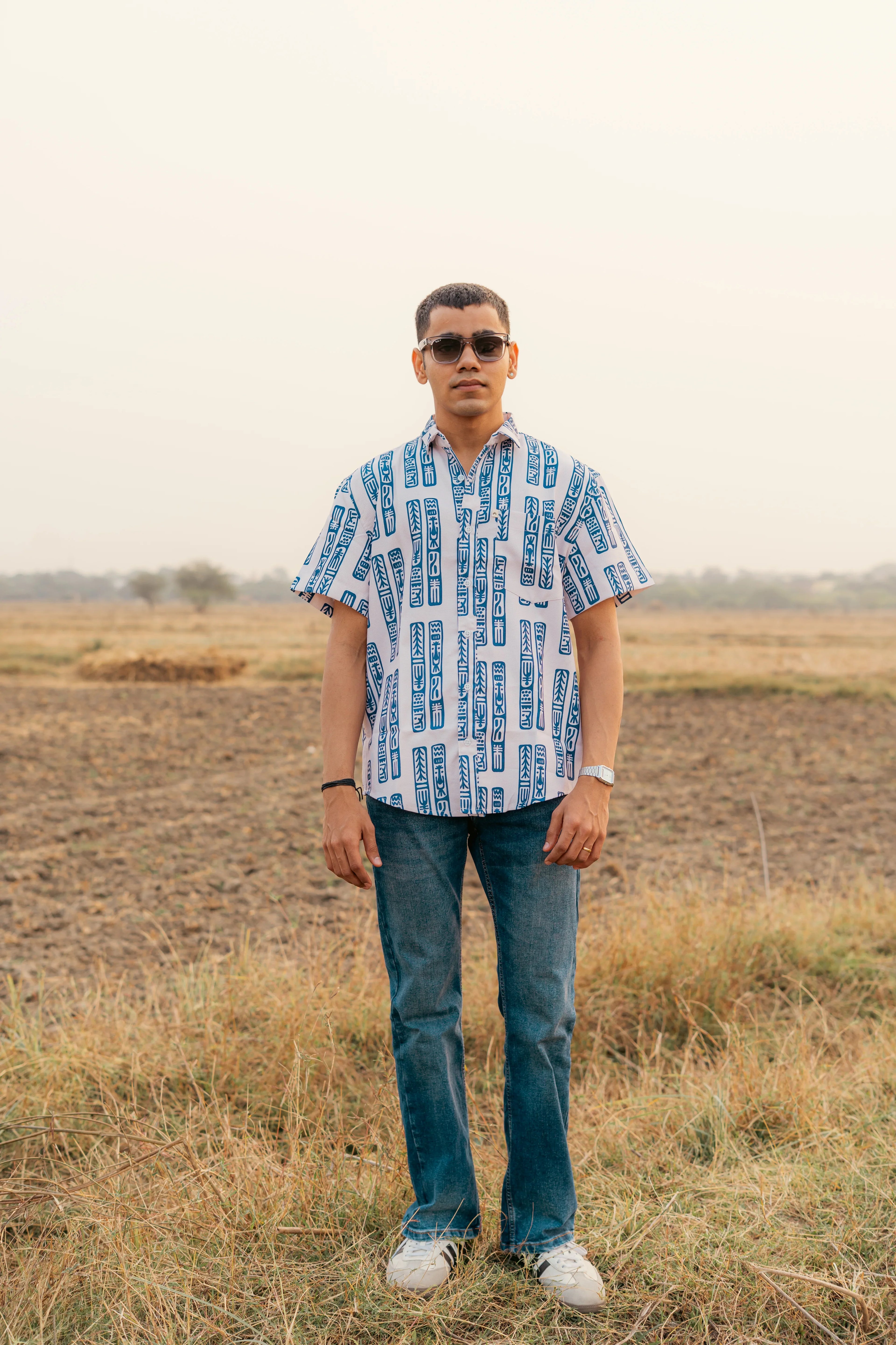 Man in modern short sleeve patterned shirt, blue jeans, sunglasses, outdoors in a field