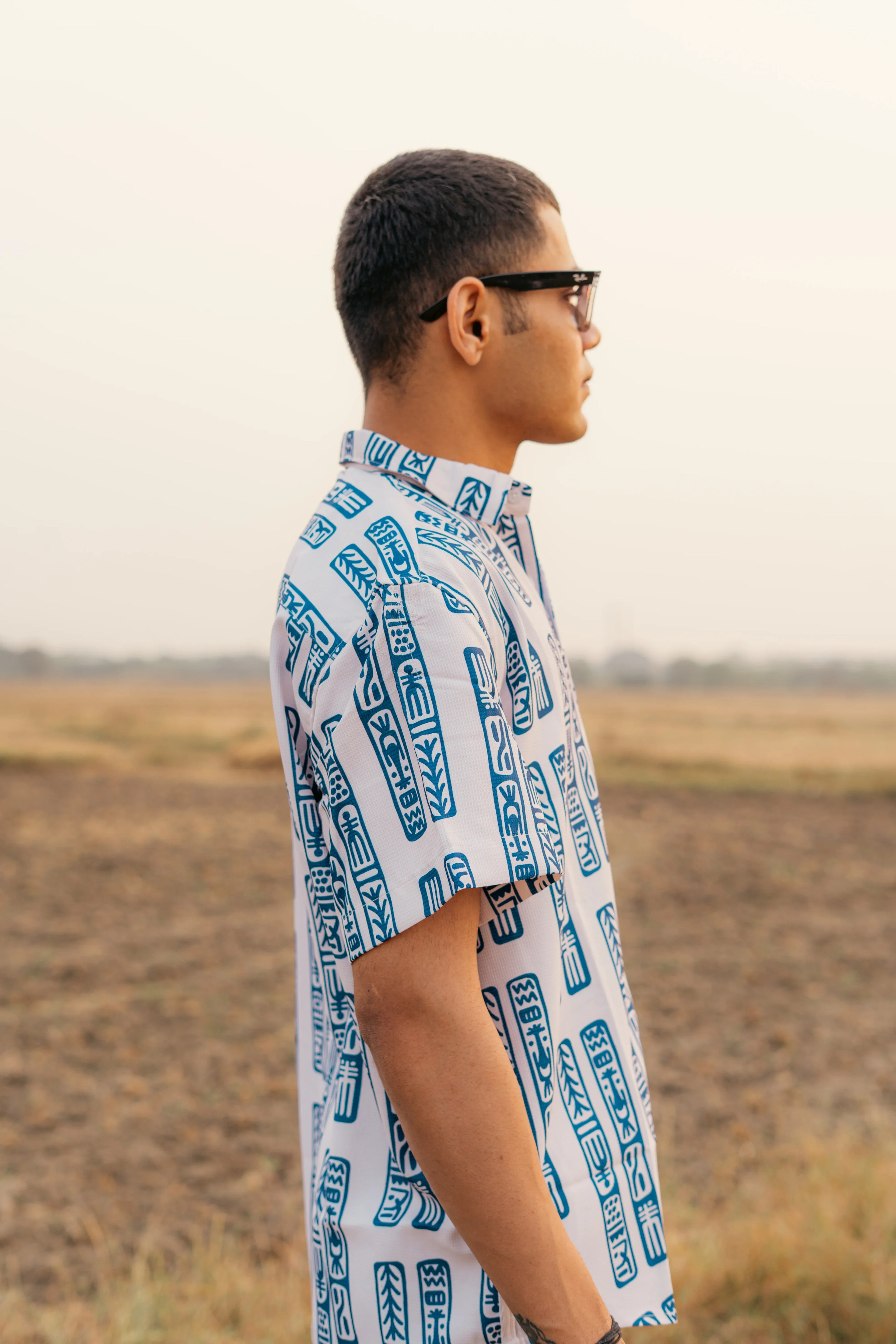 Man in sunglasses wearing a blue and white patterned short sleeve shirt outdoors