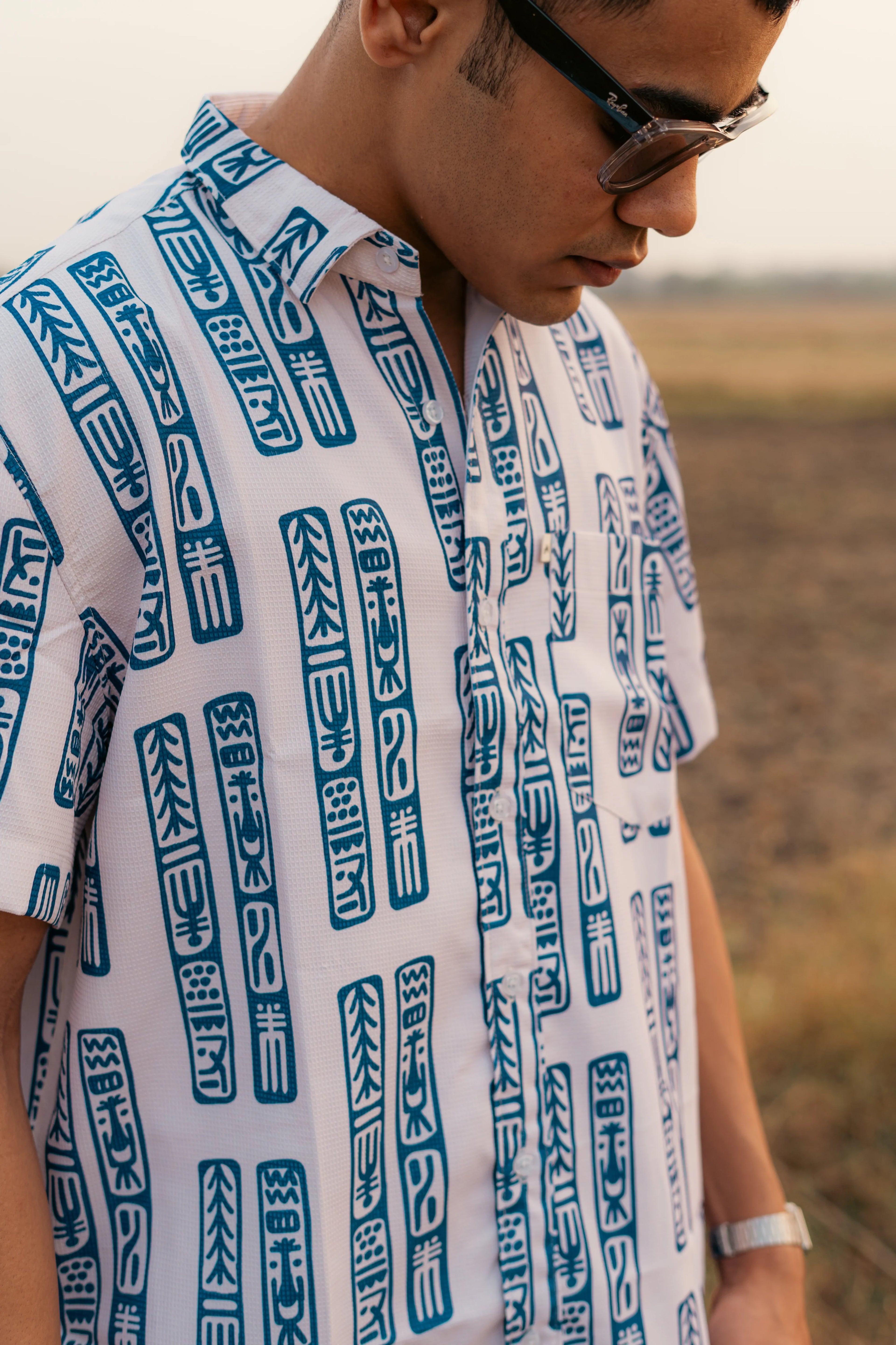 Man outdoors wearing a white short sleeve shirt with blue geometric pattern