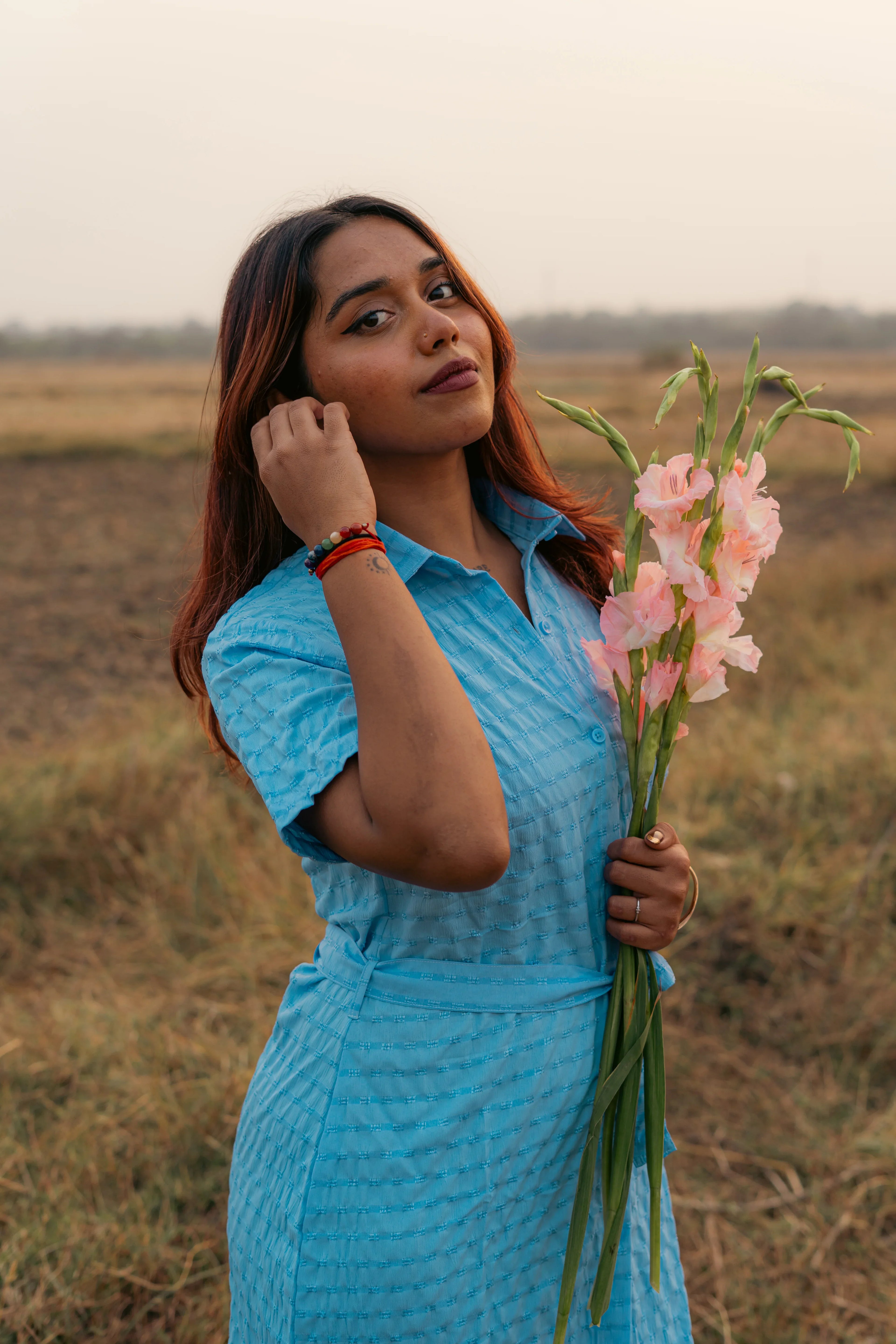 Woman in a blue textured dress holding pink flowers standing in a grassy field