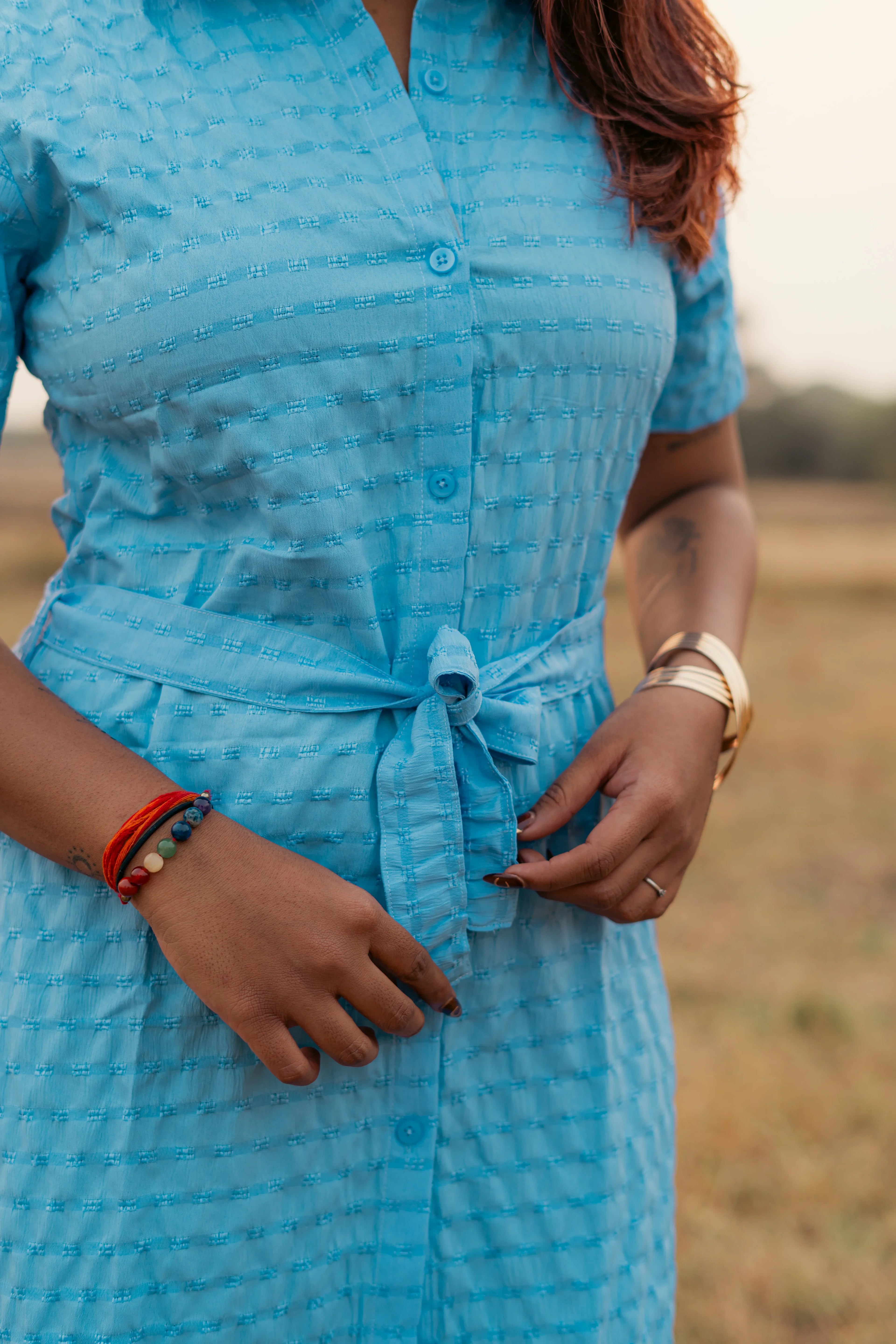 Close-up of woman wearing a textured blue button-up dress with waist tie and bracelets