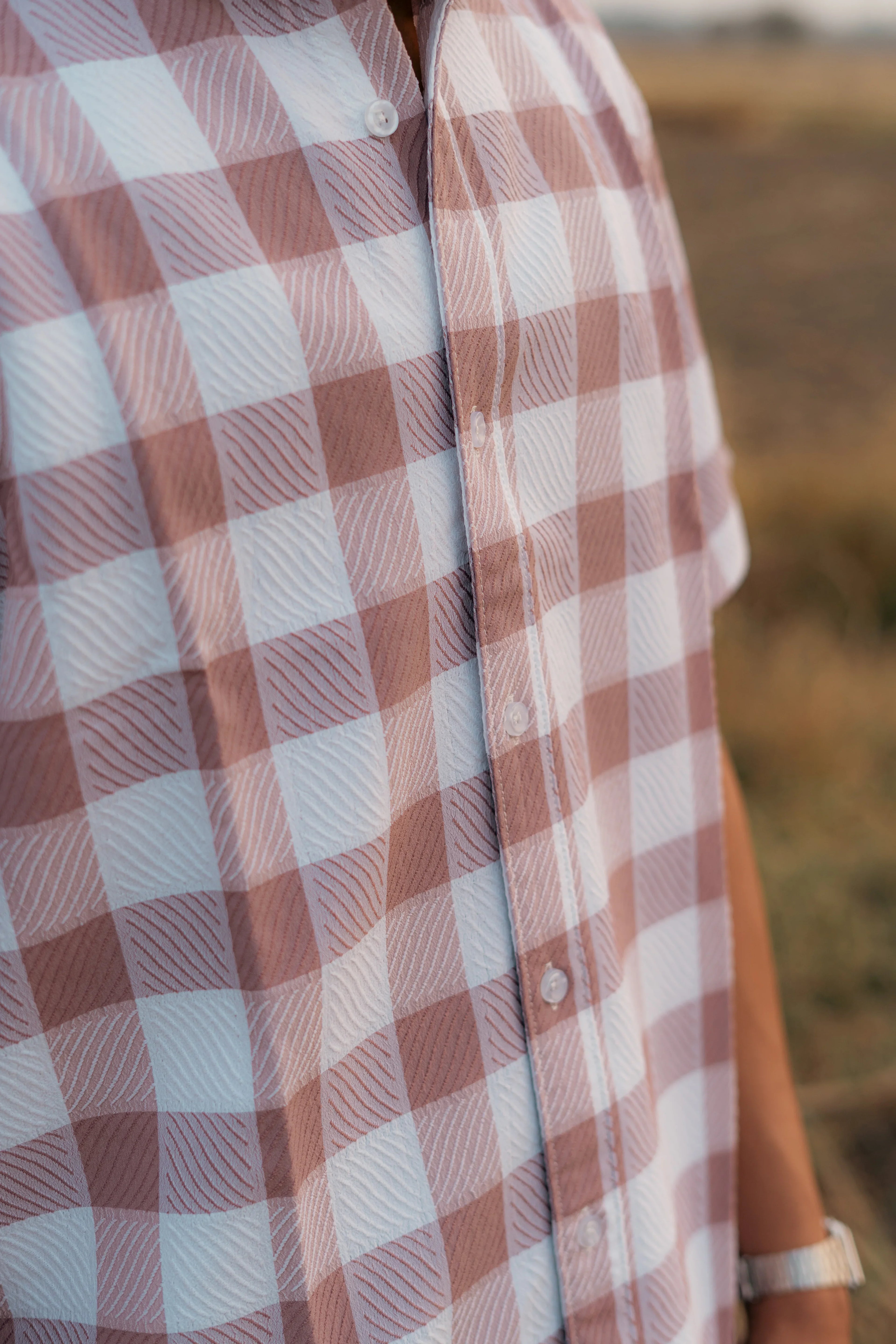 Close-up of a textured checkered short-sleeve shirt in white and light brown outdoors