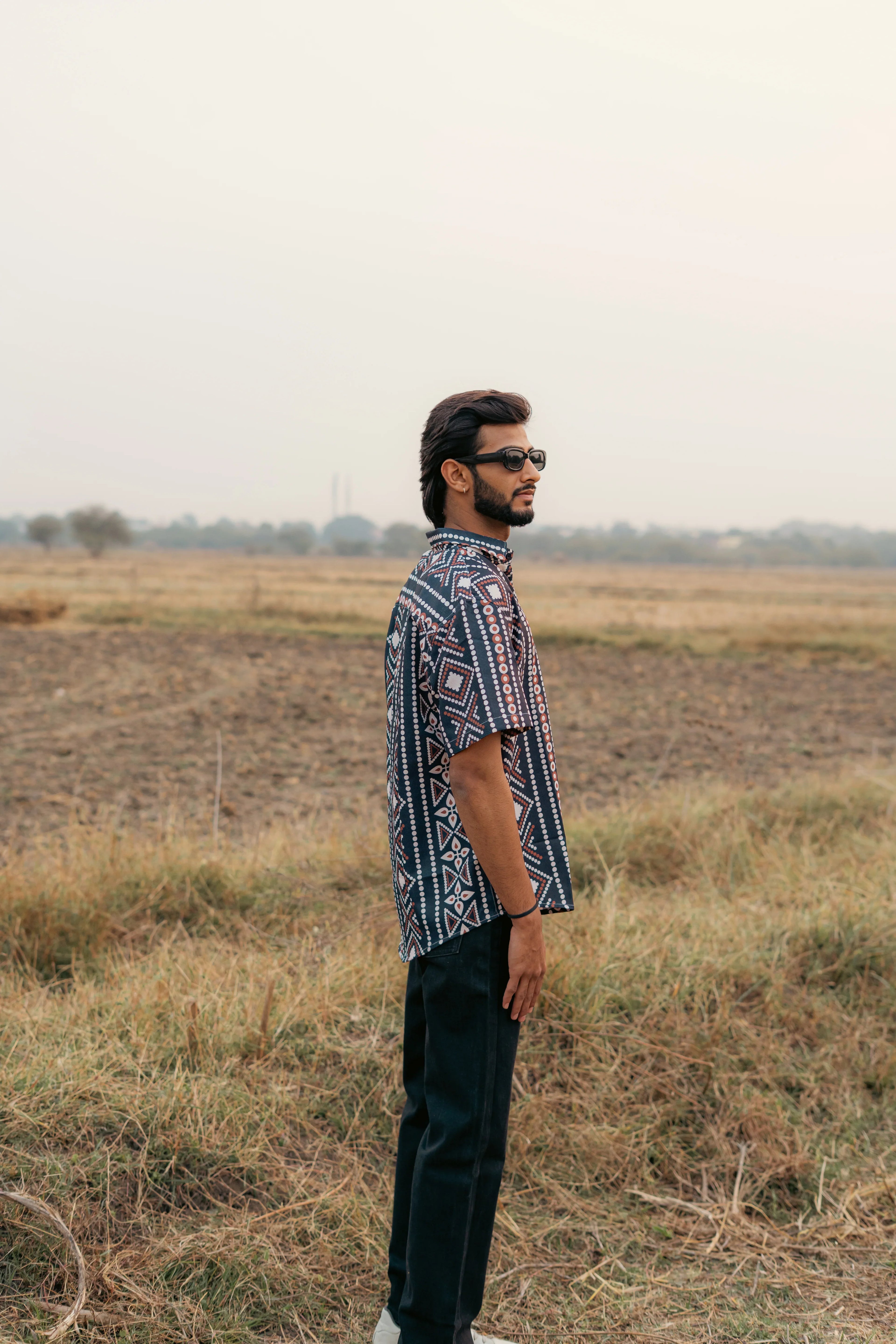 Man in patterned short sleeve shirt and sunglasses standing in a grassy field