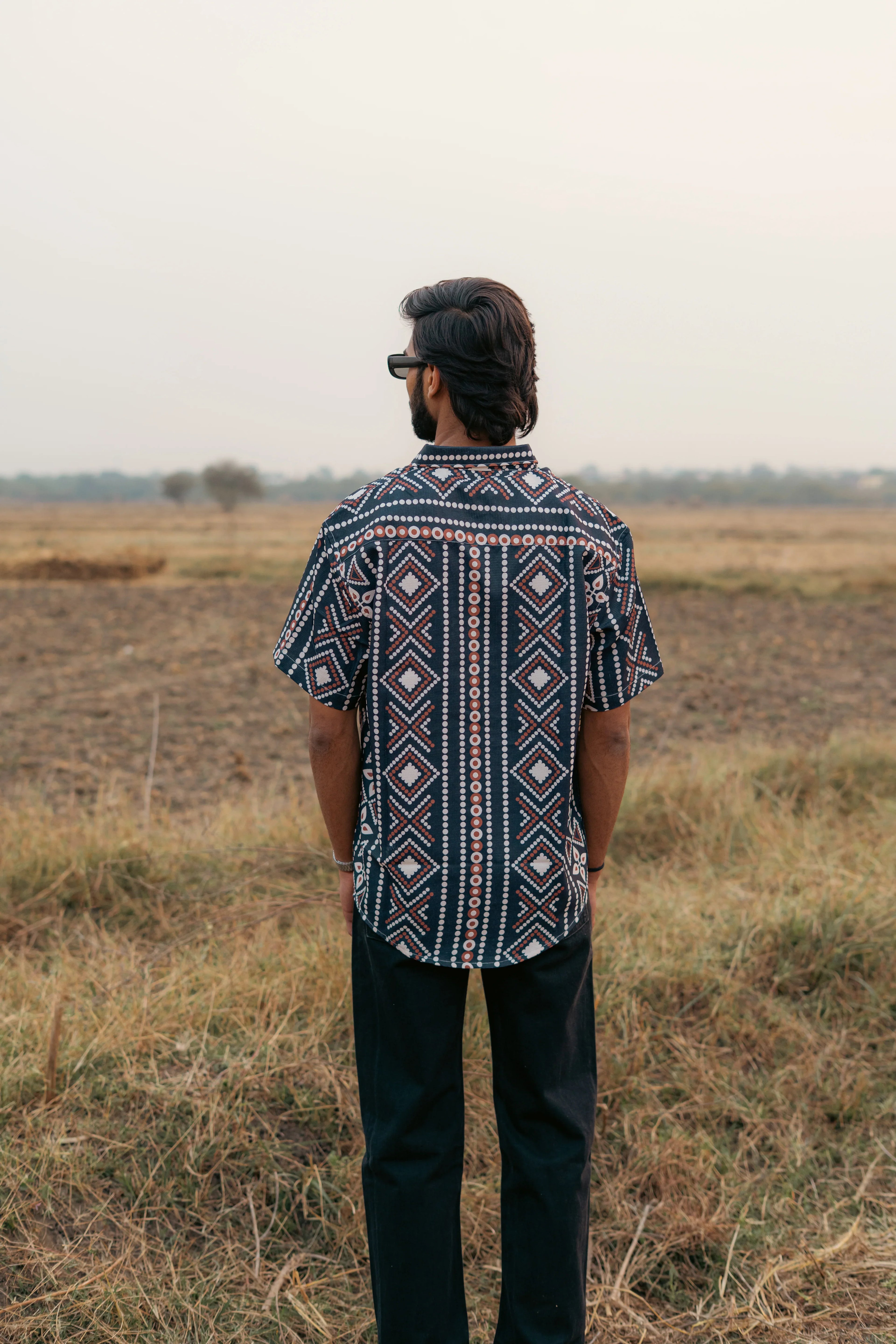 Man in geometric patterned short sleeve shirt and black pants standing in a field