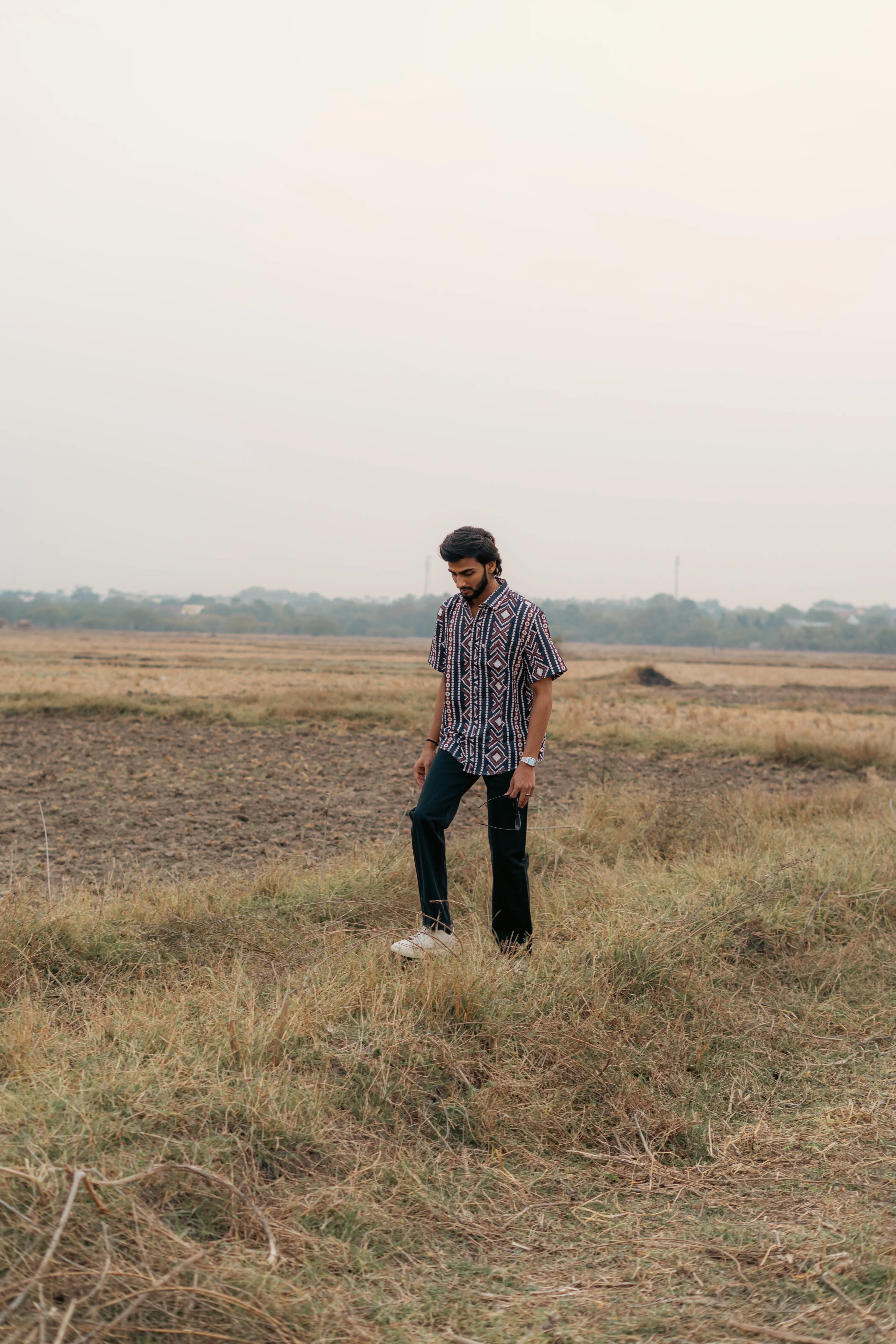 Man in patterned short sleeve shirt and dark pants standing in an open grassy field