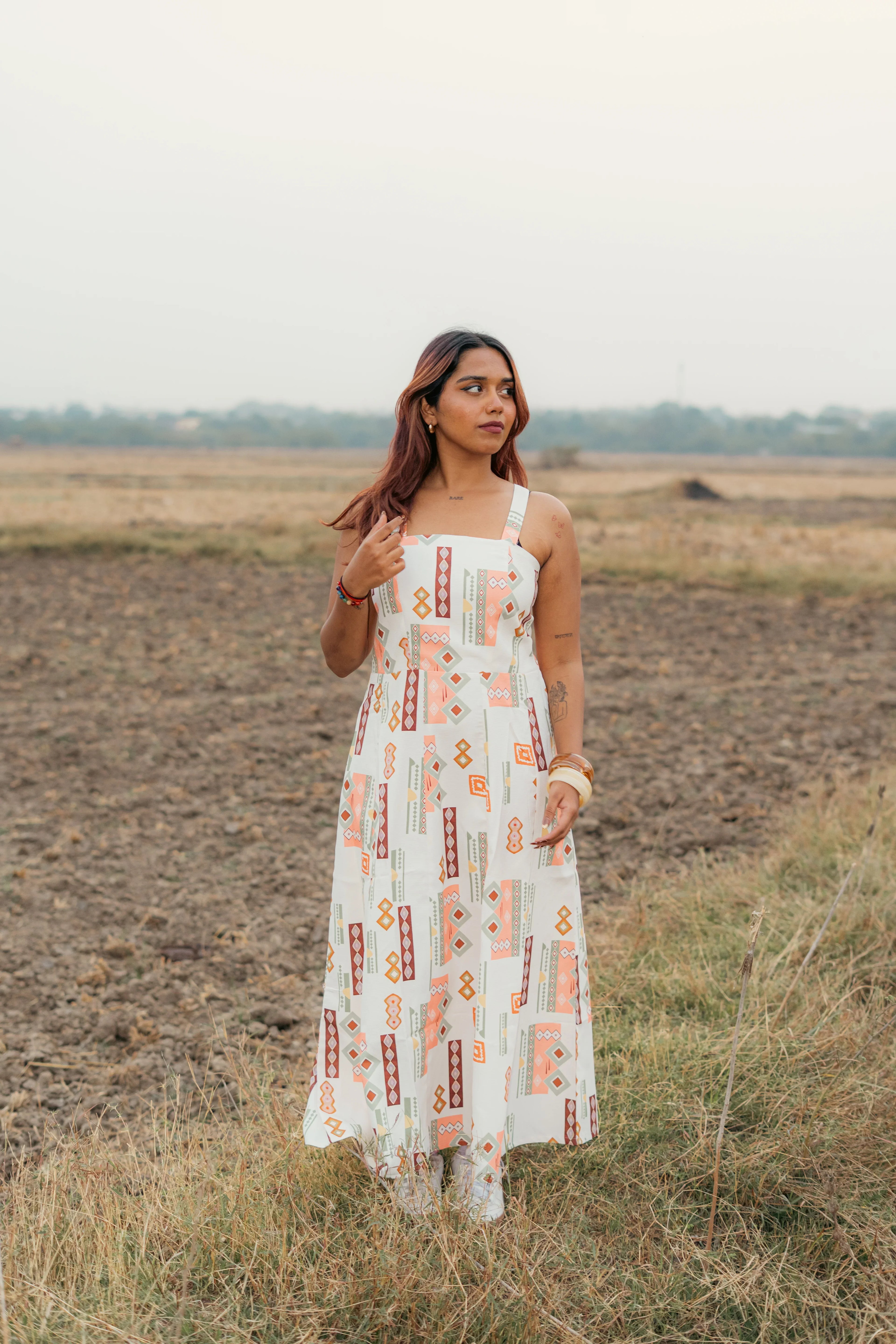 Woman in a sleeveless geometric print maxi dress standing in an open field