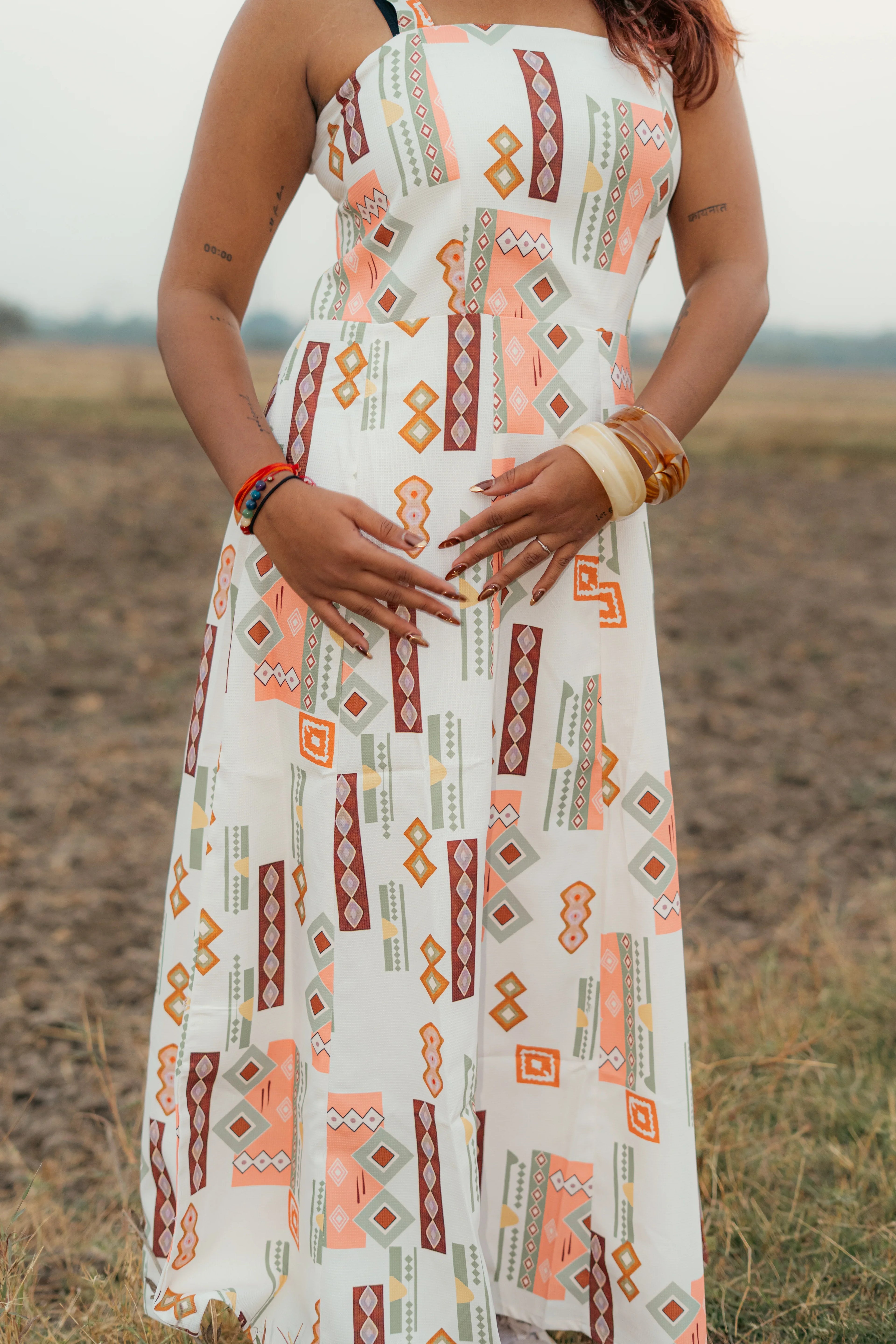 Woman in sleeveless geometric print dress standing outdoors on grass