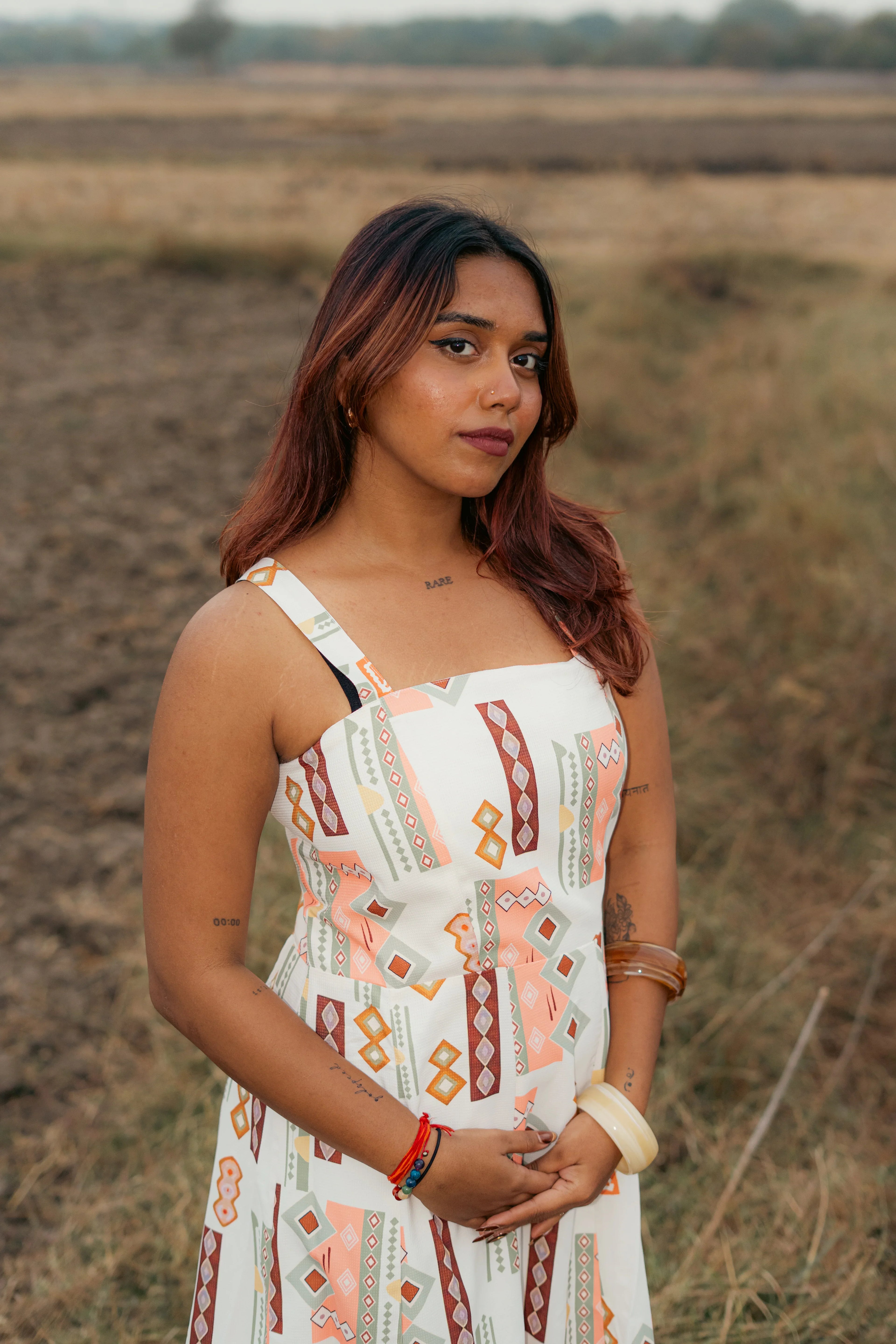 Woman in a sleeveless, geometric print dress standing outdoors in a grassy field