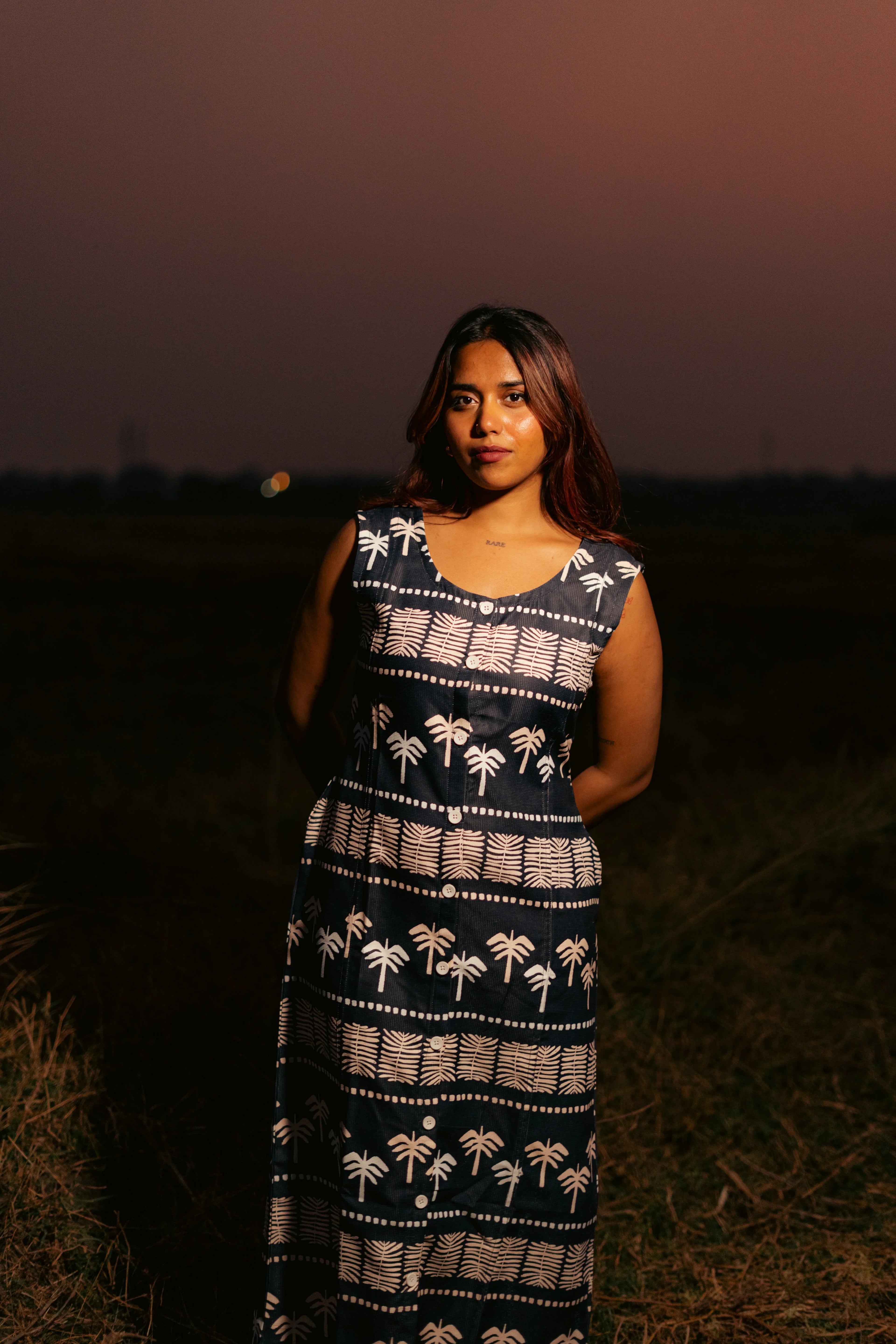 Woman in sleeveless palm print maxi dress standing outdoors at sunset