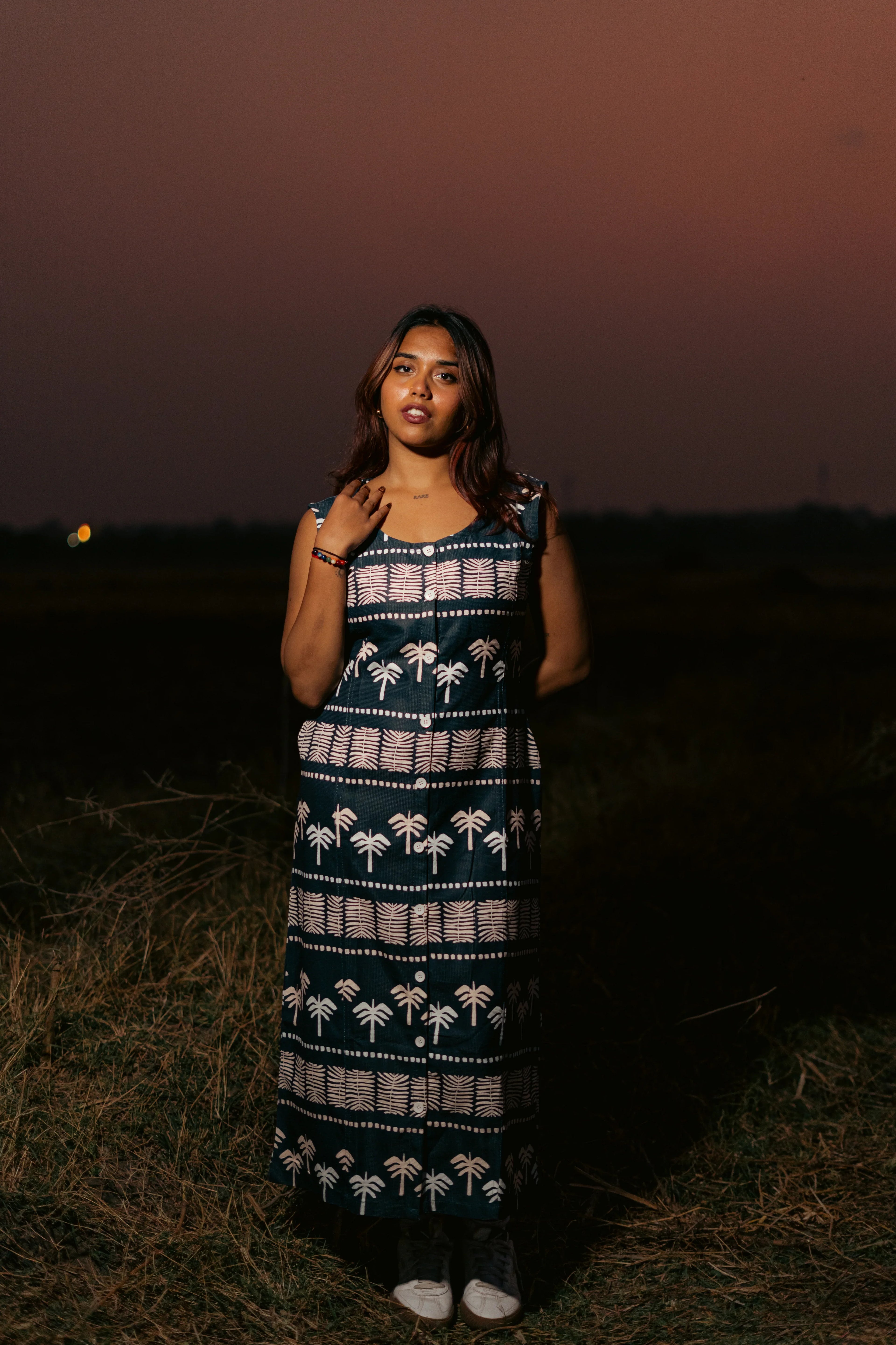 Woman in patterned sleeveless maxi dress standing in a field at sunset