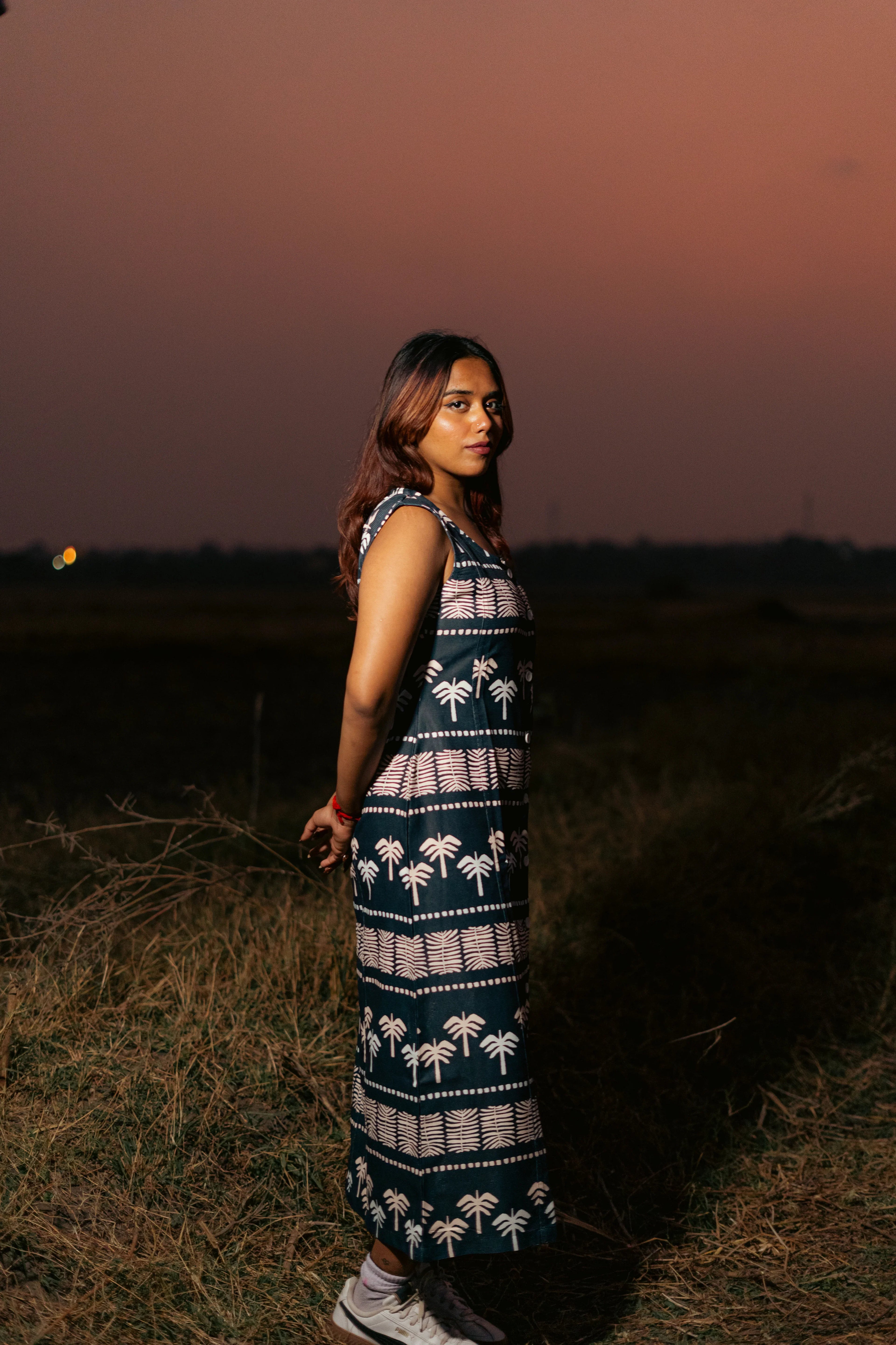 Woman in a patterned sleeveless maxi dress standing outdoors at sunset