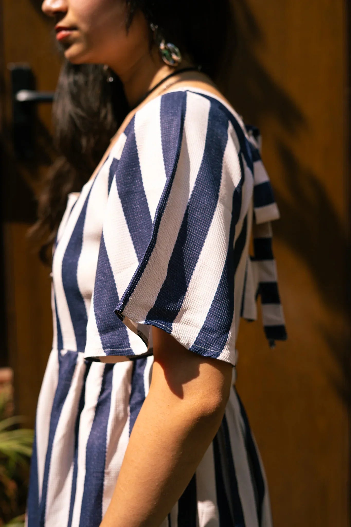 Woman in blue and white striped short sleeve dress, side view, outdoor setting