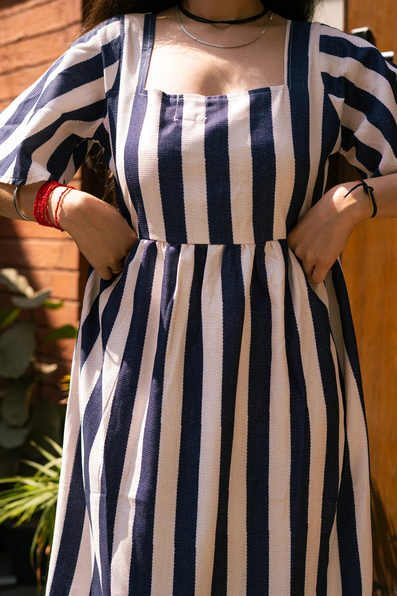 Woman wearing a blue and white striped dress with square neckline and short sleeves outdoors
