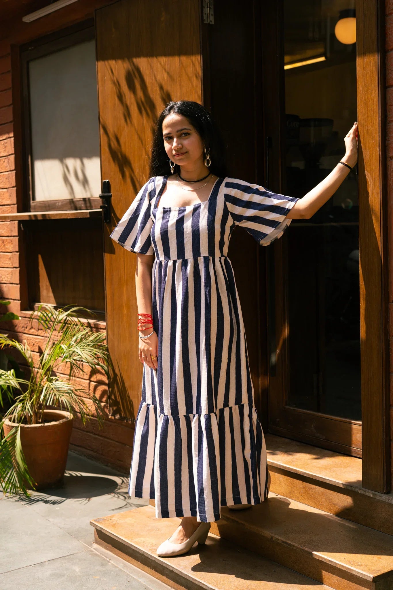 Woman in a navy and white vertical striped maxi dress standing by a wooden door