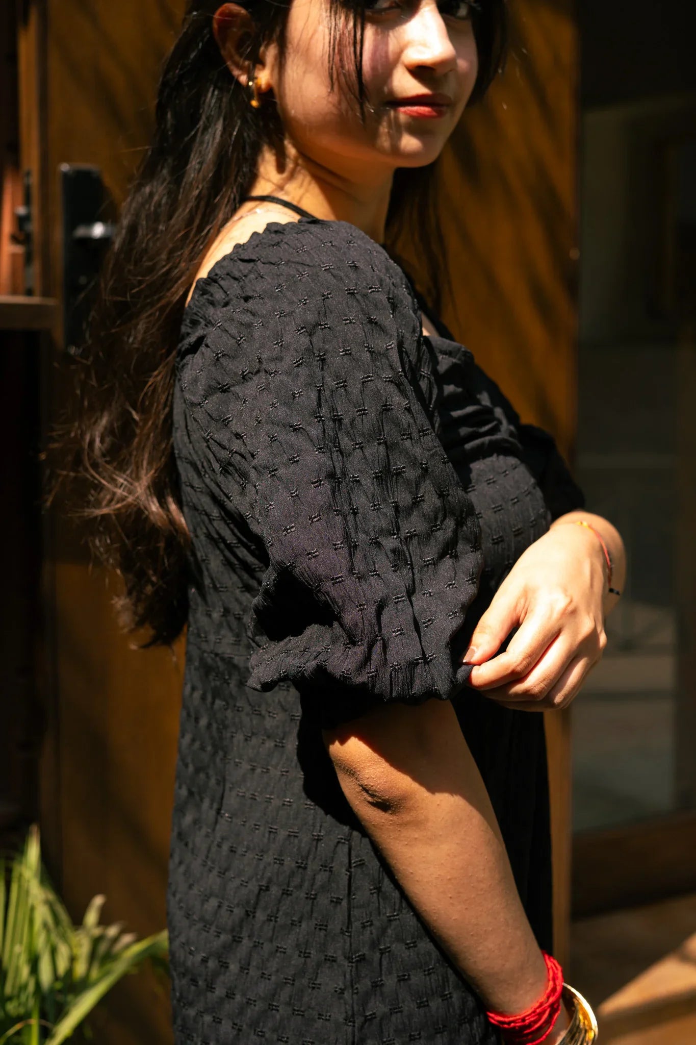 Woman in textured black puff sleeve dress with gold and red bracelets outdoors