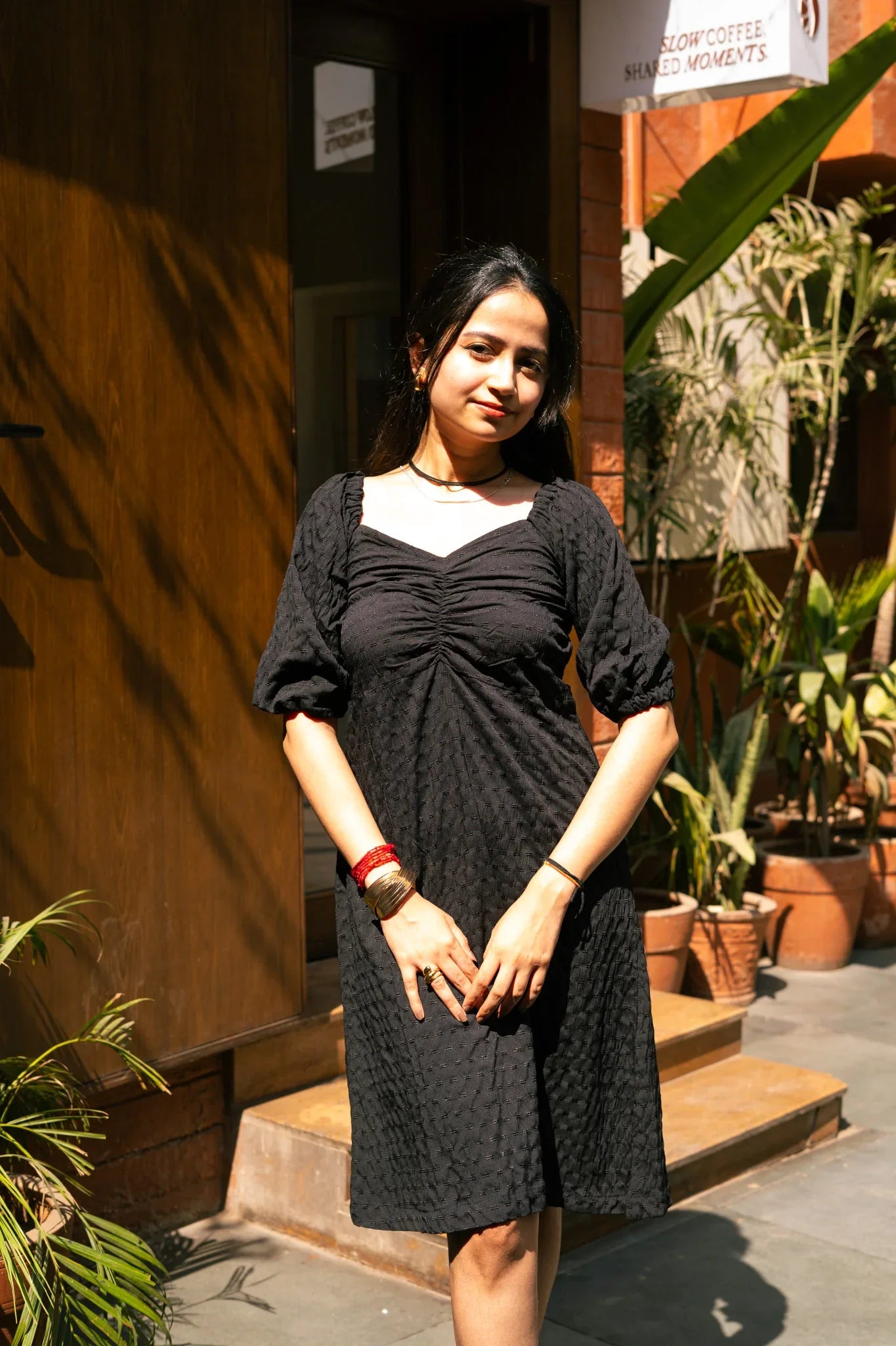 Woman outdoors wearing black textured midi dress with puff sleeves, standing in sunlight