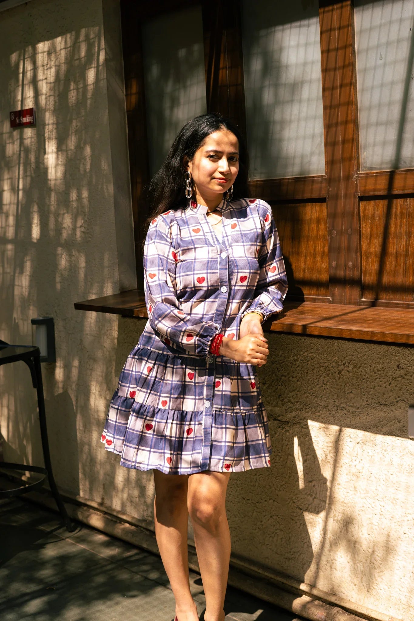 Woman wearing a long-sleeve plaid dress with red heart pattern, standing outdoors in sunlight