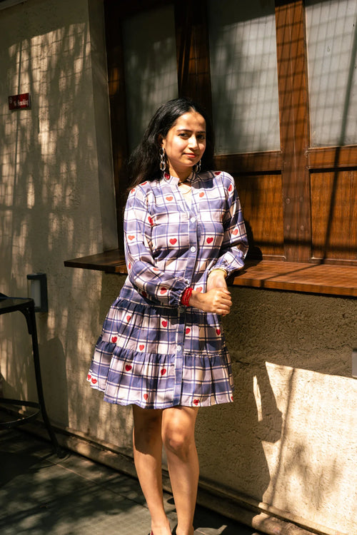 Woman wearing a long-sleeve plaid dress with red heart pattern, standing outdoors in sunlight