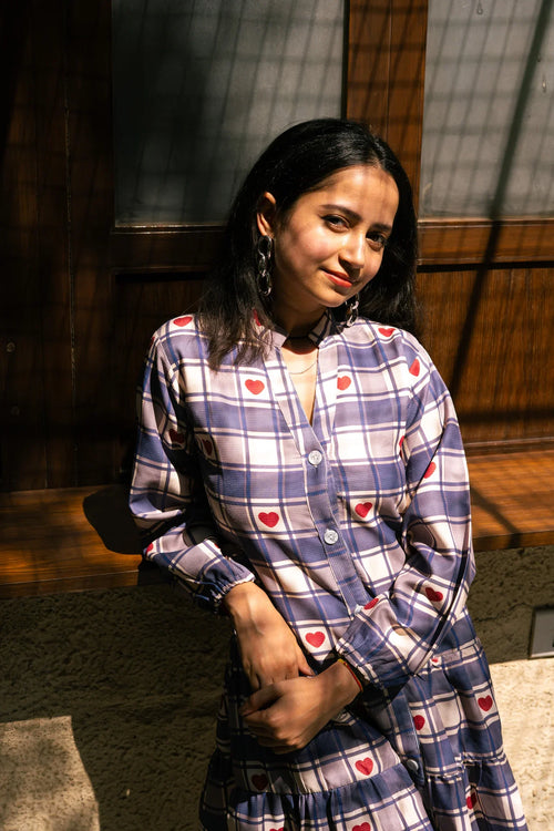 Woman in a plaid shirt dress with red heart patterns, standing in sunlight