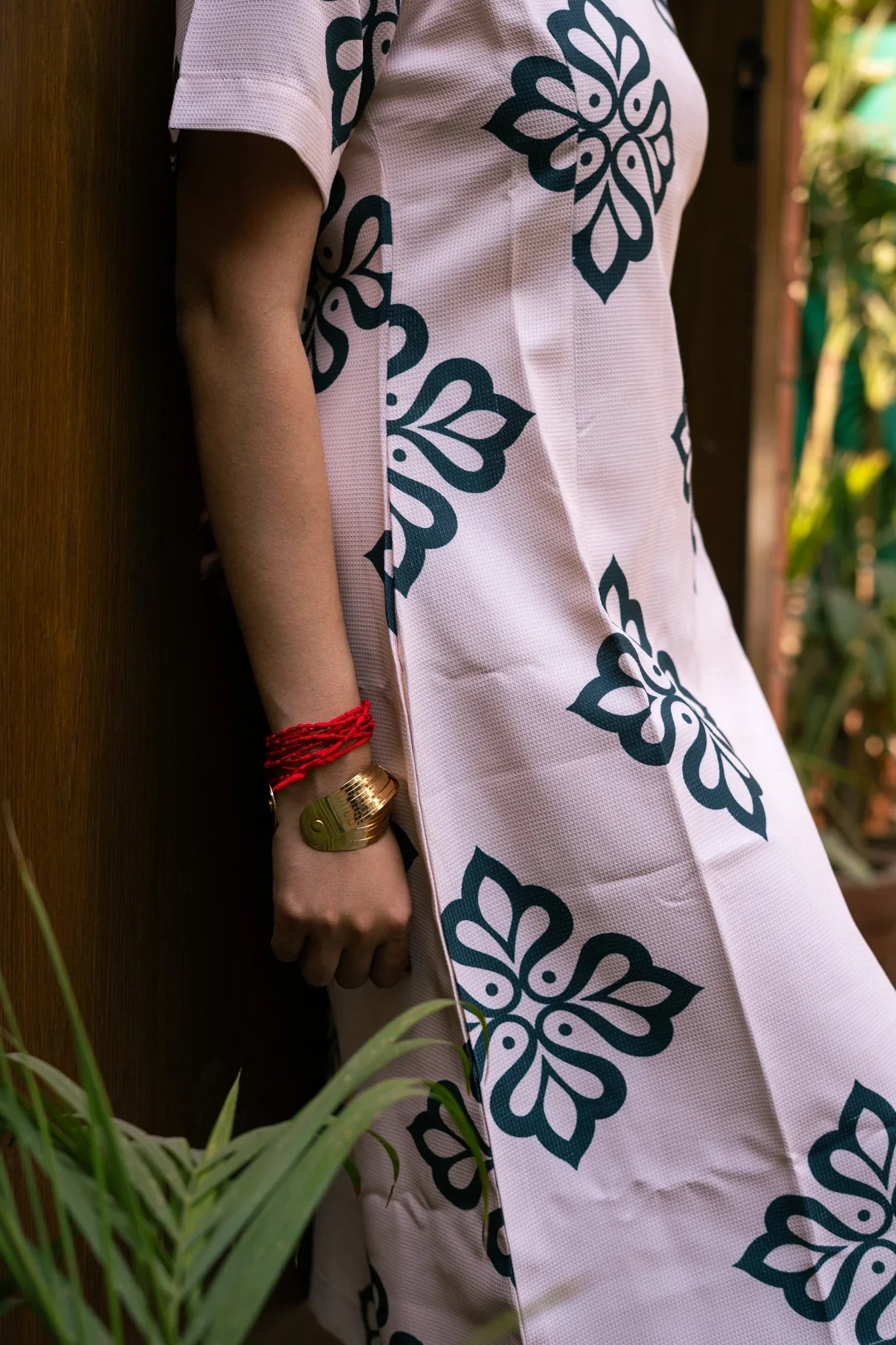 Woman in light pink dress with bold floral print, gold cuff bracelet and red thread