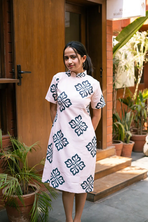 Woman wearing a white dress with black floral patterns standing outdoors.